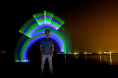 Rear view of man standing against illuminated lights at night