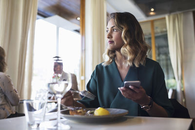 Businesswoman looking away while using mobile phone while sitting in restaurant