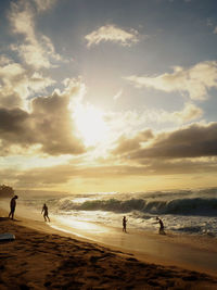 People at beach against sky during sunset