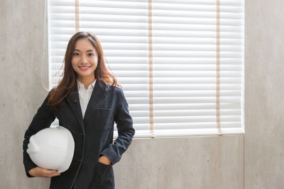 Portrait of a smiling young woman standing against window