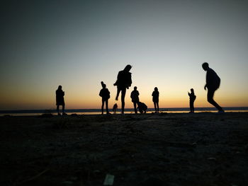 Silhouette people playing on beach against clear sky