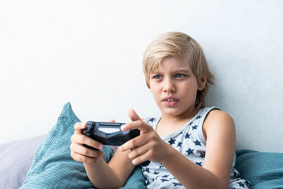 Boy holding joystick gaming controller in hands, playing video game at home.