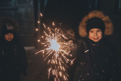 Boy holds a sparkler in his hands while celebrating a new year on the street at night.