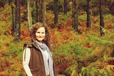 Portrait of happy young woman standing against trees in forest