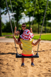 A young child with a woman on the swing in a playground