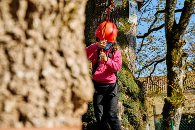 Little girl with protections practicing climbing between trees with ropes and nets