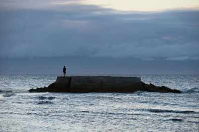 Man standing on rock formation in sea against sky
