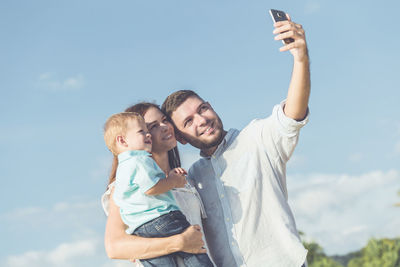Family taking selfie through mobile phone while standing against sky