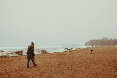 Rear view of couple walking on beach against clear sky