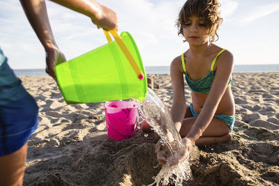 Boy pouring water on sister's hands while making sand castle at beach