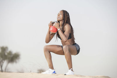 Full length of woman exercising in desert against sky