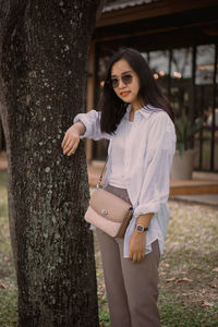 Young woman standing against tree trunk