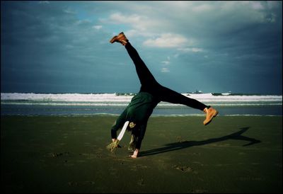 Full length of woman performing handstand on beach against sky