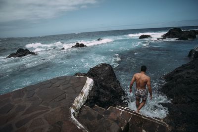 Rear view of shirtless man looking at sea against sky