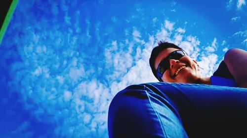 Low angle view of man using mobile phone against blue sky