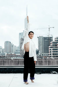 Full length portrait of smiling man standing in city against sky