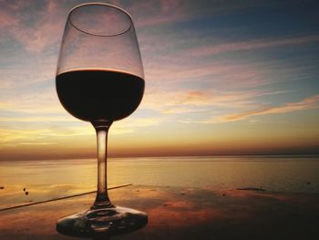 Close-up of beer on table against sea during sunset