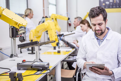 Engineer using tablet in factory with industrial robots