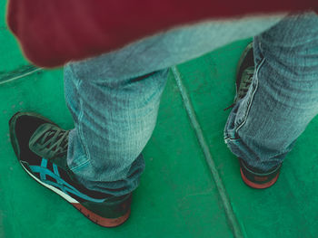 Low section of man standing on green shoe