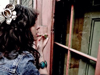 Side view of young woman applying lipstick outside old house