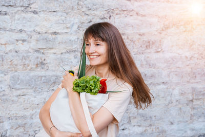 Portrait of young woman holding ice cream against wall