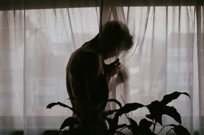 Side view of shirtless man standing by curtain at home