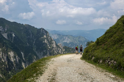 Rear view of people walking on road amidst mountains against sky