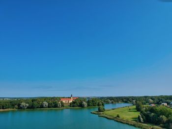 Scenic view of river by buildings against clear blue sky