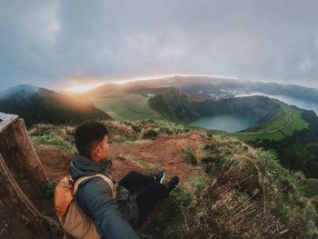 Man looking at lake while sitting on mountain against sky