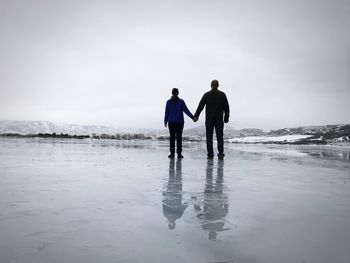 Rear view of friends walking on beach against sky