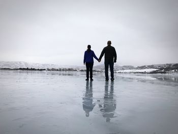 Rear view of man and woman holding hands on frozen lake against sky