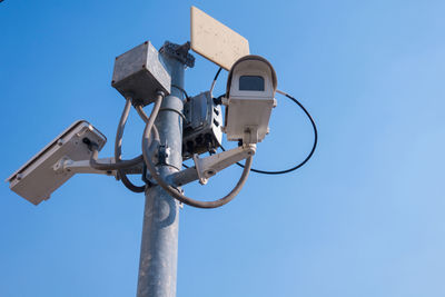 Low angle view of security camera against clear blue sky