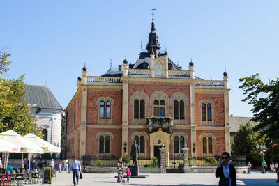 People walking in front of historic building against sky