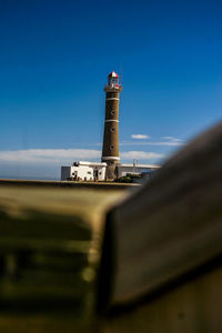 Low angle view of lighthouse by passage of wood against sky