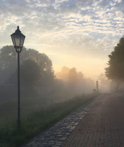 Street light by footpath against sky during sunset