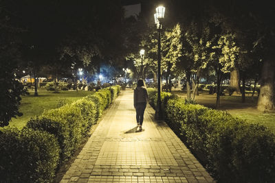 Rear view of woman walking on footpath by street at night