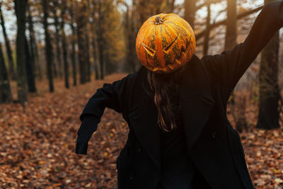 Woman wearing jack o lantern while standing in forest during autumn