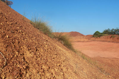 Dirt road passing through field against clear blue sky