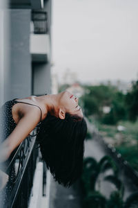 Side view of young woman leaning on balcony railing