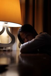 Close-up of depressed woman resting by lamp in bedroom