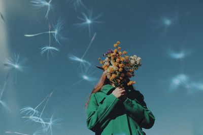 Low angle view of person holding flowering plant against sky