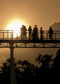 Silhouette people standing on bridge against clear sky during sunset