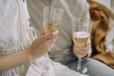 Midsection of couple holding champagne flutes while sitting at home