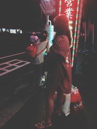Rear view of woman standing on street at night