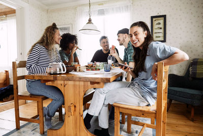 Portrait of smiling young woman using smart phone while sitting with friends at home