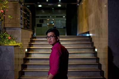 Portrait of young man standing on staircase at night