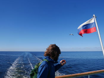 Side view of man standing by russian flag in boat on sea