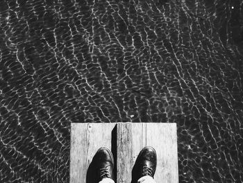 Low section of man standing on wooden plank over lake