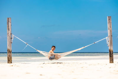 Rear view of woman sitting on beach against clear blue sky