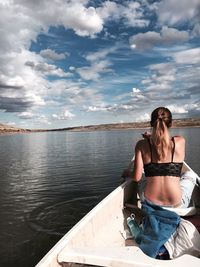 Rear view of sensuous woman sitting in boat over river against sky